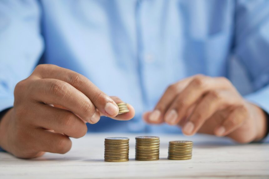 Hand placing a coin into a glass jar labeled investing representing micro asset growth