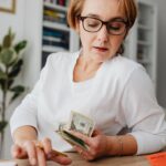 A smiling woman at a desk organizing finances and personal budgeting & saving strategies with a laptop and ledgers.